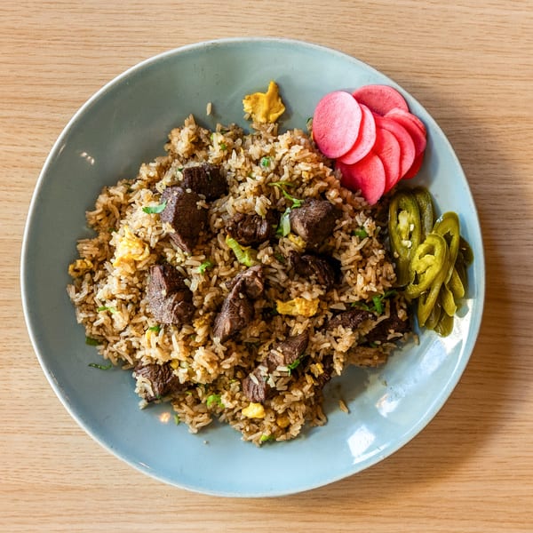 Peruvian fried rice with beef, scrambled egg, pickled radishes, and jalapeños on a blue plate.