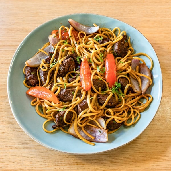 Peruvian Lomo Saltado with noodles, beef, red onions, and tomatoes on a blue plate.