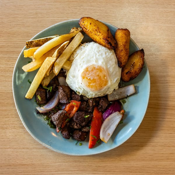 Peruvian Lomo Saltado with steak, fries, fried egg, plantains, red onions, and peppers.