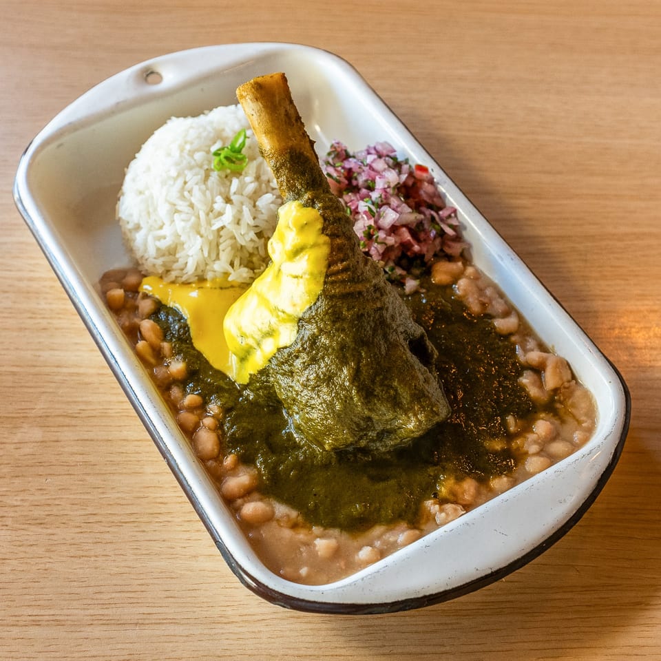 Peruvian seco de cordero, a lamb shank with green sauce, white rice, beans, and red onion salsa.