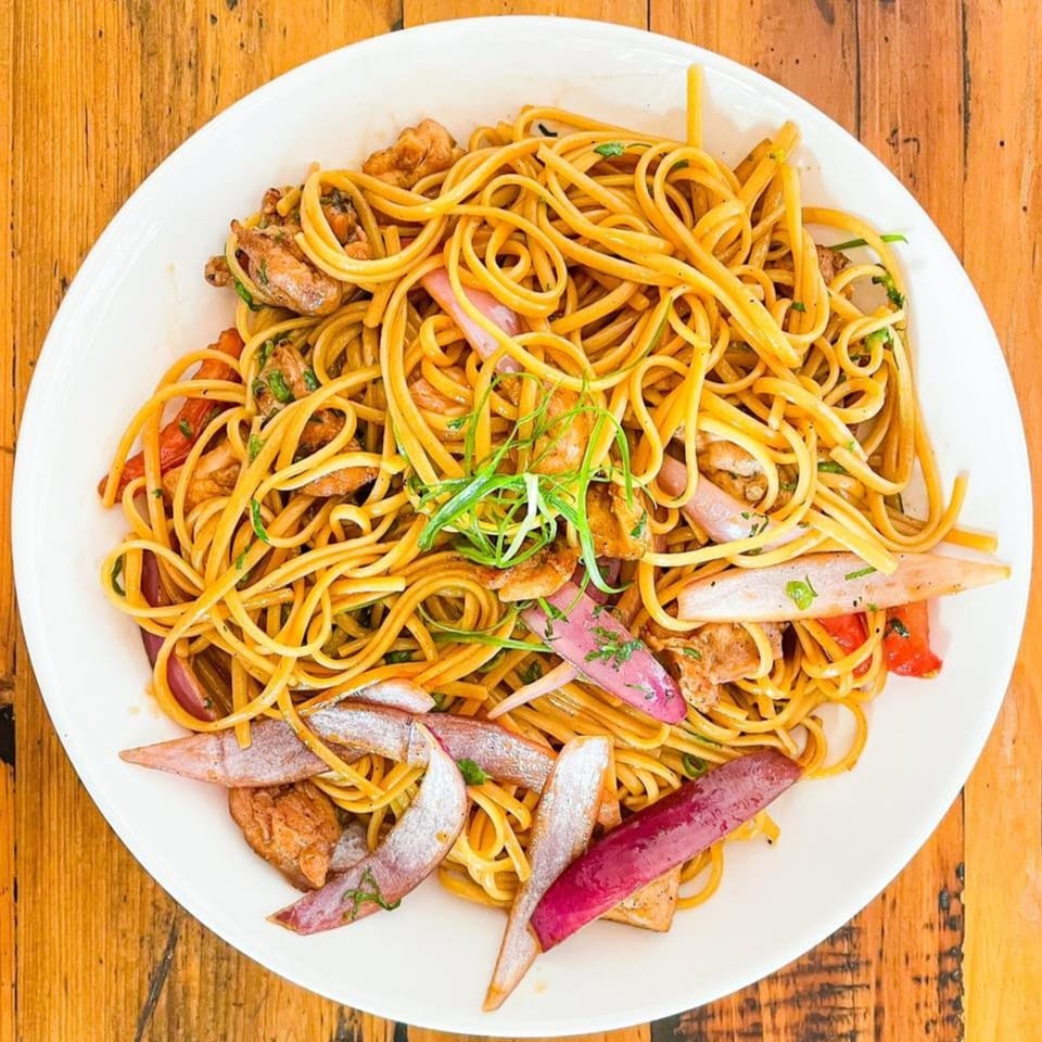 Peruvian Lomo Saltado with noodles, chicken, red onions, and green onions on a white plate.