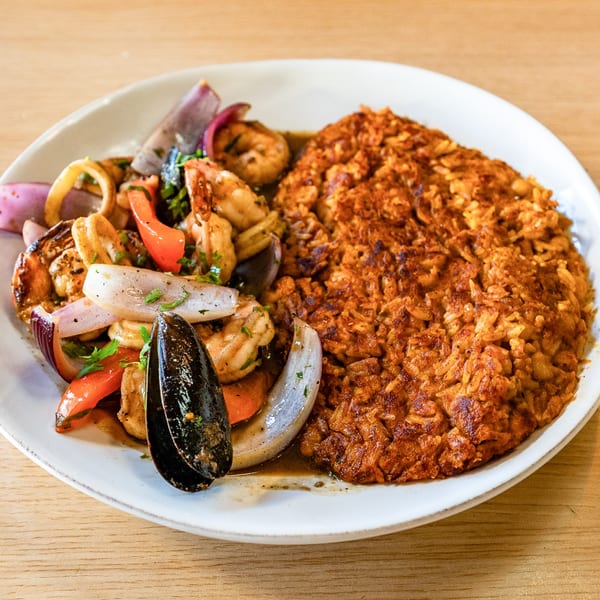 Peruvian seafood dish with shrimp, mussels, squid, red onions, and peppers next to seasoned rice.