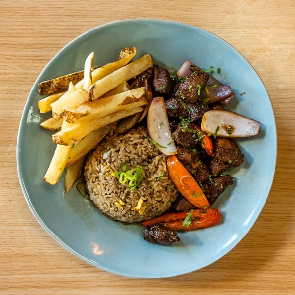 Picante's Lomo Saltado with steak, fries, rice, onions, and carrots on a blue plate.