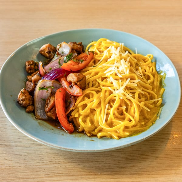 Peruvian Lomo Saltado with chicken, red onions, tomatoes, and peppers, served with yellow noodles.