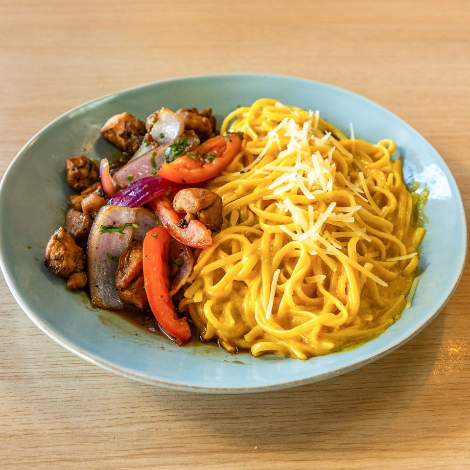Peruvian Lomo Saltado with chicken, red onions, tomatoes, and peppers, served with yellow noodles.