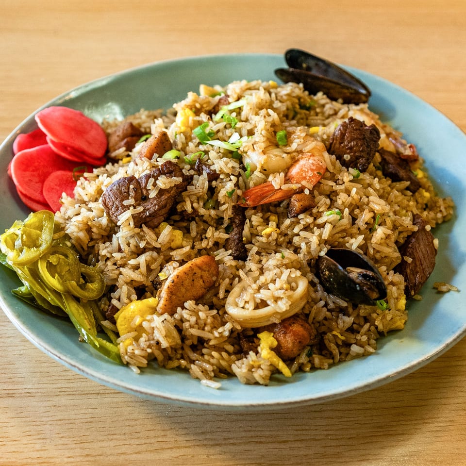 Peruvian chaufa rice with seafood, beef, and chicken, garnished with pickled vegetables.