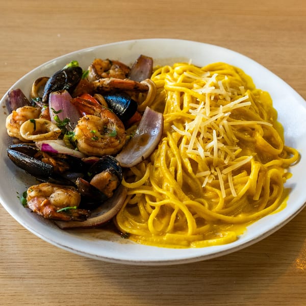 Peruvian seafood pasta with mussels, shrimp, squid, red onions, and yellow noodles with cheese.