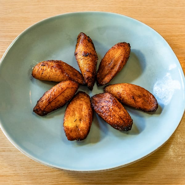 Seven golden-brown fried plantains, arranged in a circle on a light blue plate, on a wooden table.