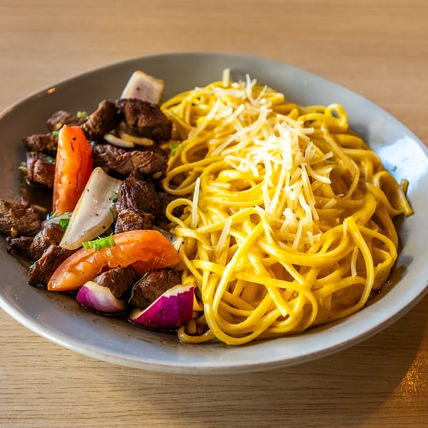 Peruvian Lomo Saltado with beef, tomatoes, onions, and a side of cheesy yellow noodles.